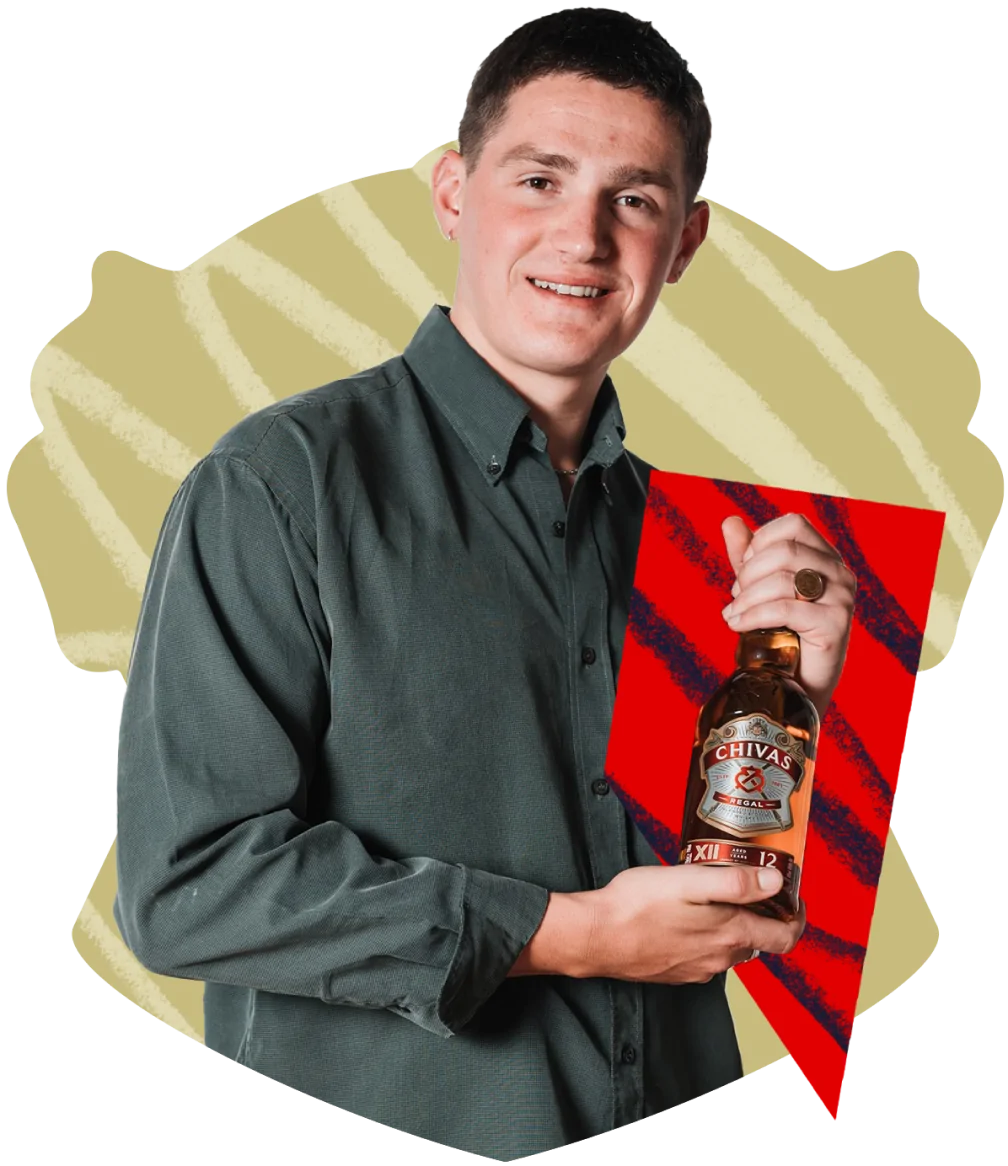 Brand Ambassador Oliver Bennion holds a bottle of Chivas Regal against a red background.